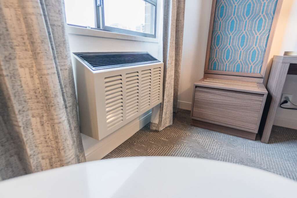 A bathroom with a window and a white air conditioner.Canadian hotel room